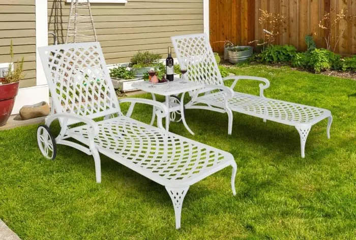 two white cast aluminum chaise lounges on the lawn in front of a house